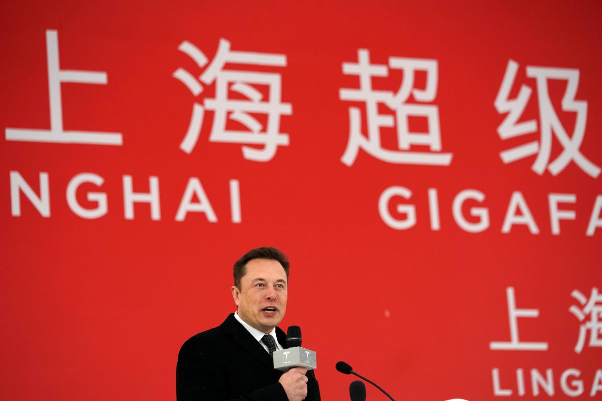 Elon Musk speaking with a microphone, with text behind him saying "Shanghai Gigafactory."