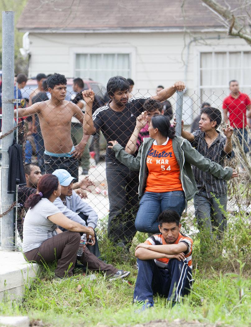 FILE - In this March 19, 2014 file photo, people wait outside a house in southeast Houston where more than 100 people in the United States illegally were discovered, according to police. Five men, at least two of them from Mexico, are accused of using guns and threats to hold 115 people hostage unless they paid ransom to continue their illegal entry into the United States. The five are scheduled to appear before a federal magistrate judge on Tuesday, March 25, 2014. (AP Photo/Houston Chronicle, Cody Duty, File)
