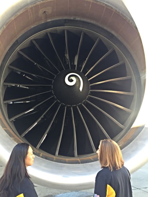 The aircraft techs pass by a plane engine.