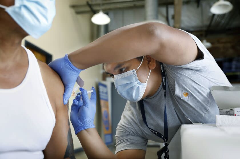 LOS ANGELES, CA - AUGUST 23, 2022: Jeremy Oyague, right, a registered nurse with The Los Angeles Department of Public Health, administers a COVID booster at a vaccination clinic to immunize people against monkeypox and COVID at The Village Mental Health Services in Los Angeles, a site run by The People Concern. (Christina House / Los Angeles Times)