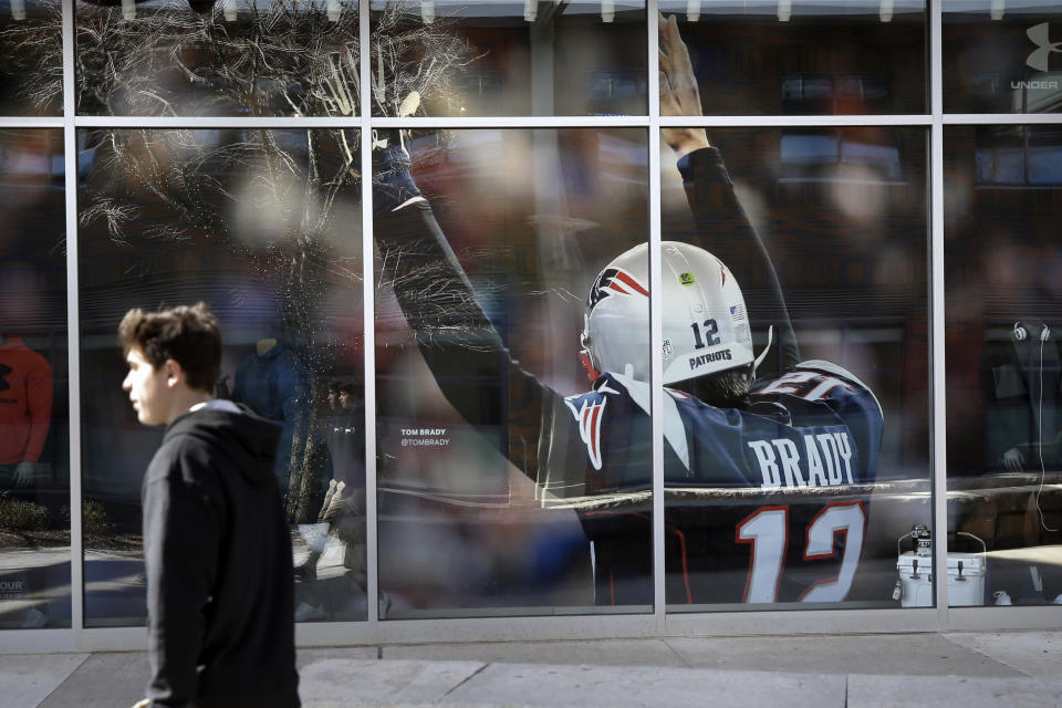 A passer-by walks past an oversized photograph of former New England Patriots football quarterback Tom Brady, Wednesday, March 18, 2020, at Patriot Place mall, in Foxborough, Mass. Brady said on social media on Tuesday, March 17, 2020 that he would not be returning to the Patriots and has become a free agent. (AP Photo/Steven Senne)