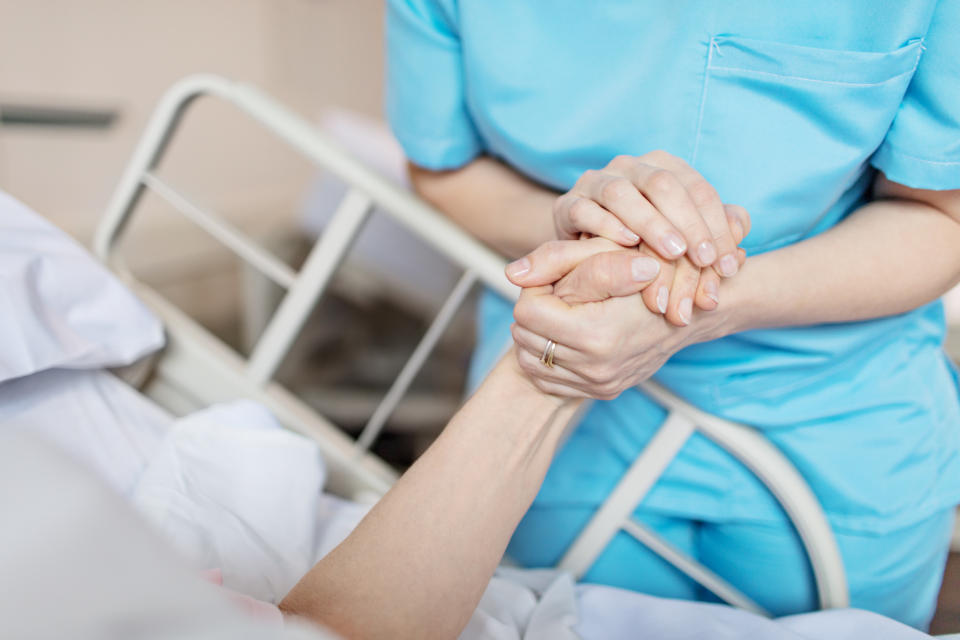 A female nurse is pictured holding senior woman's hand. 