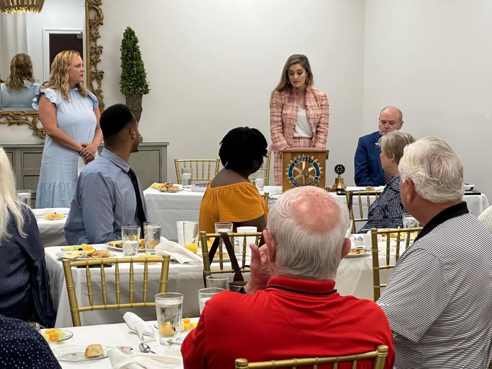 Caroline Lasseter, executive director of the Tuscaloosa Educational Foundation, in blue, and Claire Day, PR director for the Tuscaloosa Morning Rotary Club, at the podium, spoke at a meeting celebrating the return of Interact service clubs to local high schools.