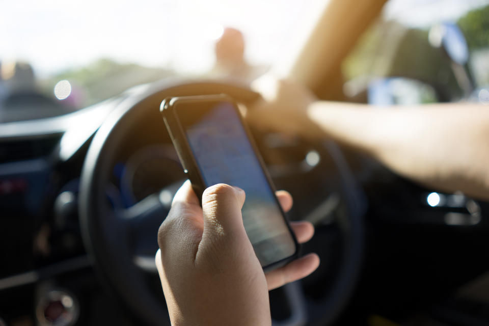 Person in a car using a smartphone with map navigation, other hand on steering wheel