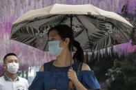 People wearing face masks to help curb the spread of the coronavirus walk by a decoration outside a shopping mall in Beijing, Sunday, June 28, 2020. China has extended COVID-19 tests to newly reopened salons amid a drop in cases while South Korea continues to face new infections as it eases social distancing rules. (AP Photo/Andy Wong)