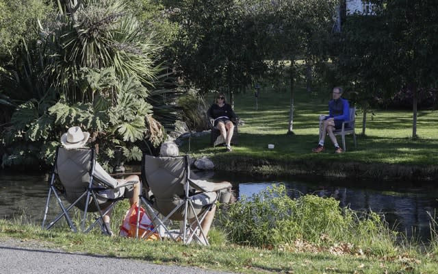 Neighbours chat across a stream as they practice social distancing in a suburb of Christchurch, New Zealand