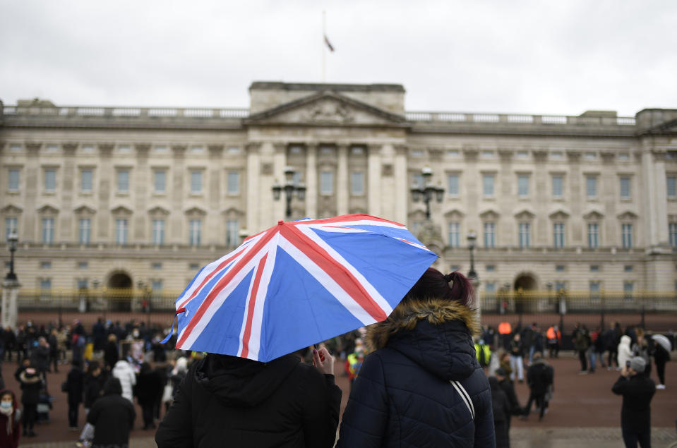A couple stand under an umbrella will the Union flag on it outside Buckingham Palace in London, a day after the death of Britain's Prince Philip, Saturday, April 10, 2021. Britain's Prince Philip, the irascible and tough-minded husband of Queen Elizabeth II who spent more than seven decades supporting his wife in a role that mostly defined his life, died on Friday. (AP Photo/Alberto Pezzali)