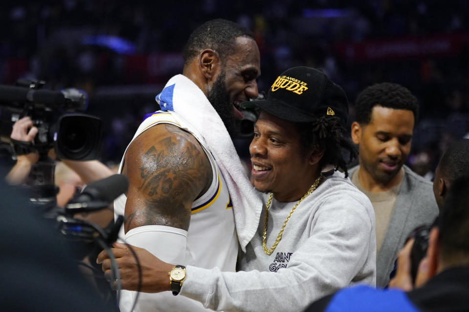 FILE - Los Angeles Lakers forward LeBron James, left, greets rapper Jay-Z after an NBA basketball game between the Los Angeles Clippers and the Lakers, March 8, 2020, in Los Angeles. Just as a movie soundtrack helps viewers follow the action of the narrative through each plot twist, hip-hop has done the same for basketball via the NBA. It underscores how hip-hop has used the NBA to step outside its urban origins and reach every corner of the country. Once derided by mainstream America, the words and contributions of hip-hop artists now impact the masses. Jay-Z not only bought a minority a stake in the Brooklyn Nets but designed the uniforms. (AP Photo/Mark J. Terrill, file)