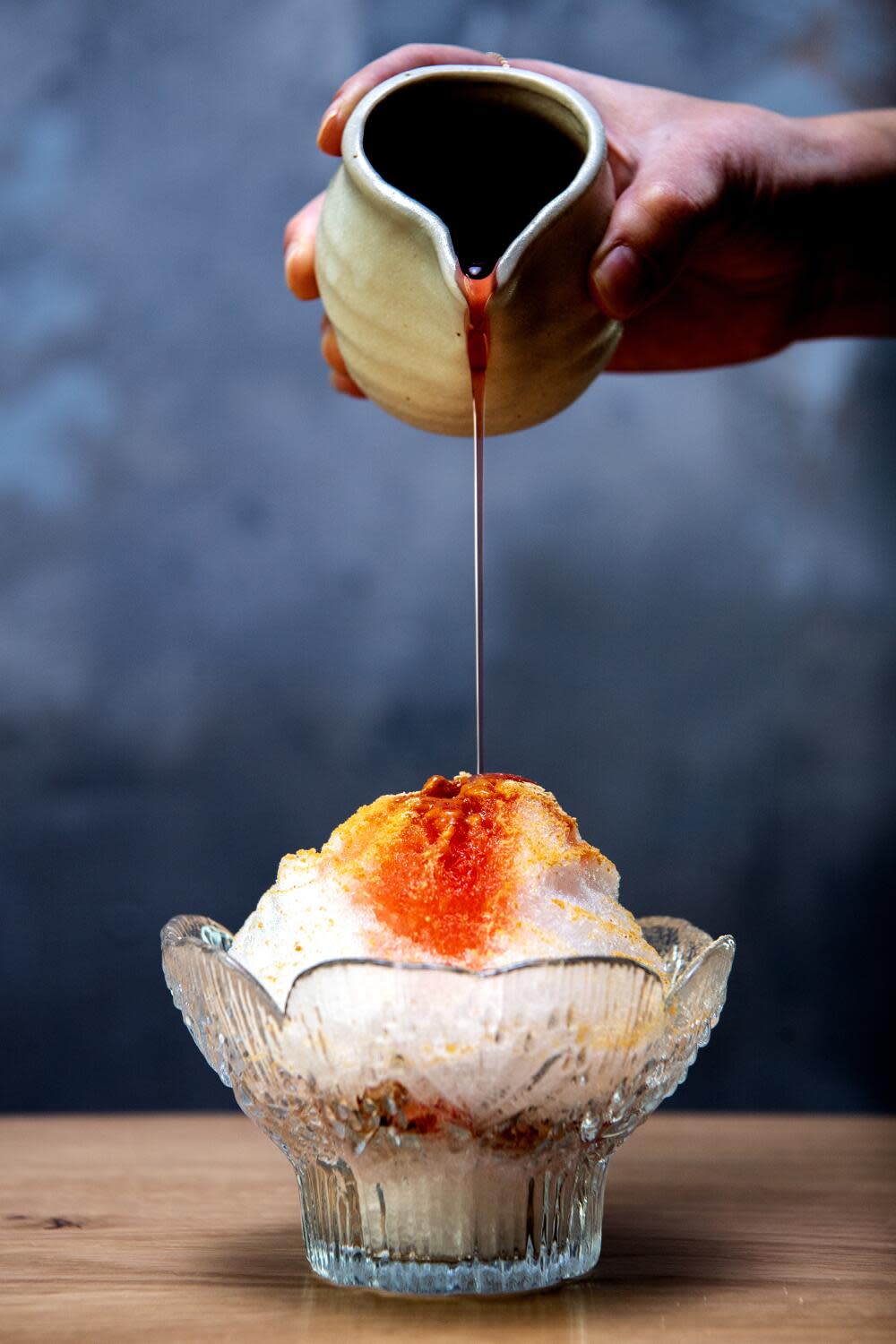 An ice desert with a hand holding a small jar above, pouring a topping.