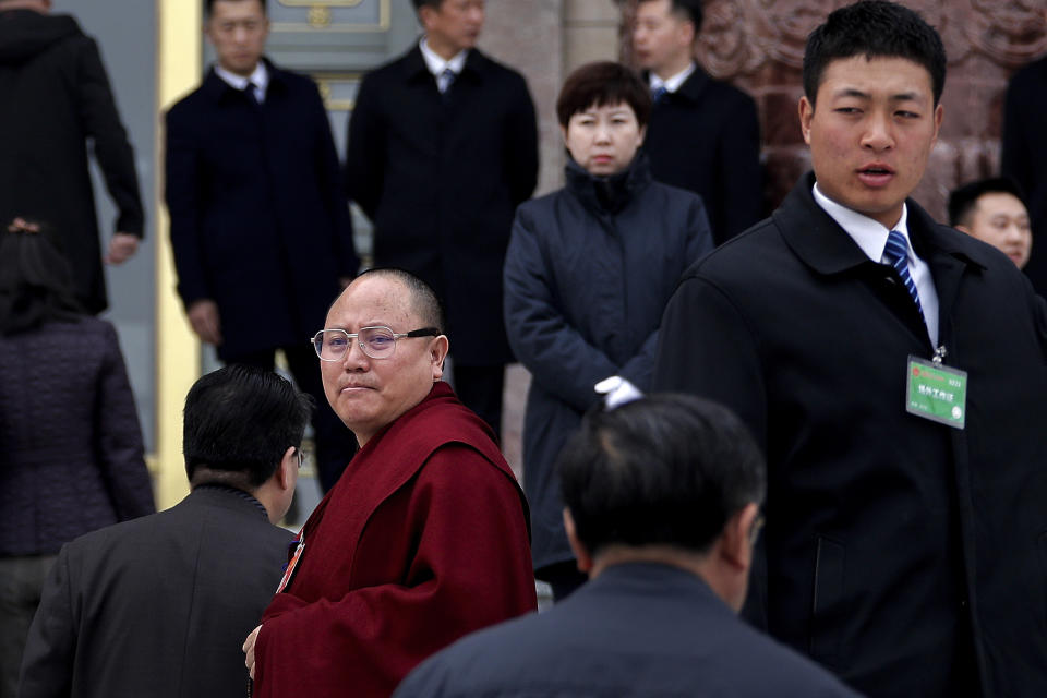 Soldiers in usher uniforms stand watch as a Tibetan monk, a delegate to the Chinese People's Political Consultative Conference (CPPCC), looks back as he and other delegates arrive to the Great Hall of the People to attend a plenary session of the CPPCC in Beijing, Sunday, March 10, 2019. China is defending its often-criticized policies toward Tibet 60 years after the Dalai Lama fled abroad amid an uprising against Chinese rule. The official Xinhua News Agency says economic growth, increases in lifespan and better education refute the claims of critics. (AP Photo/Andy Wong)