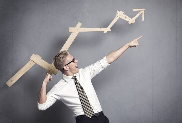 Man, in white shirt and tie, celebrating in front of wooden chart indicating gains.