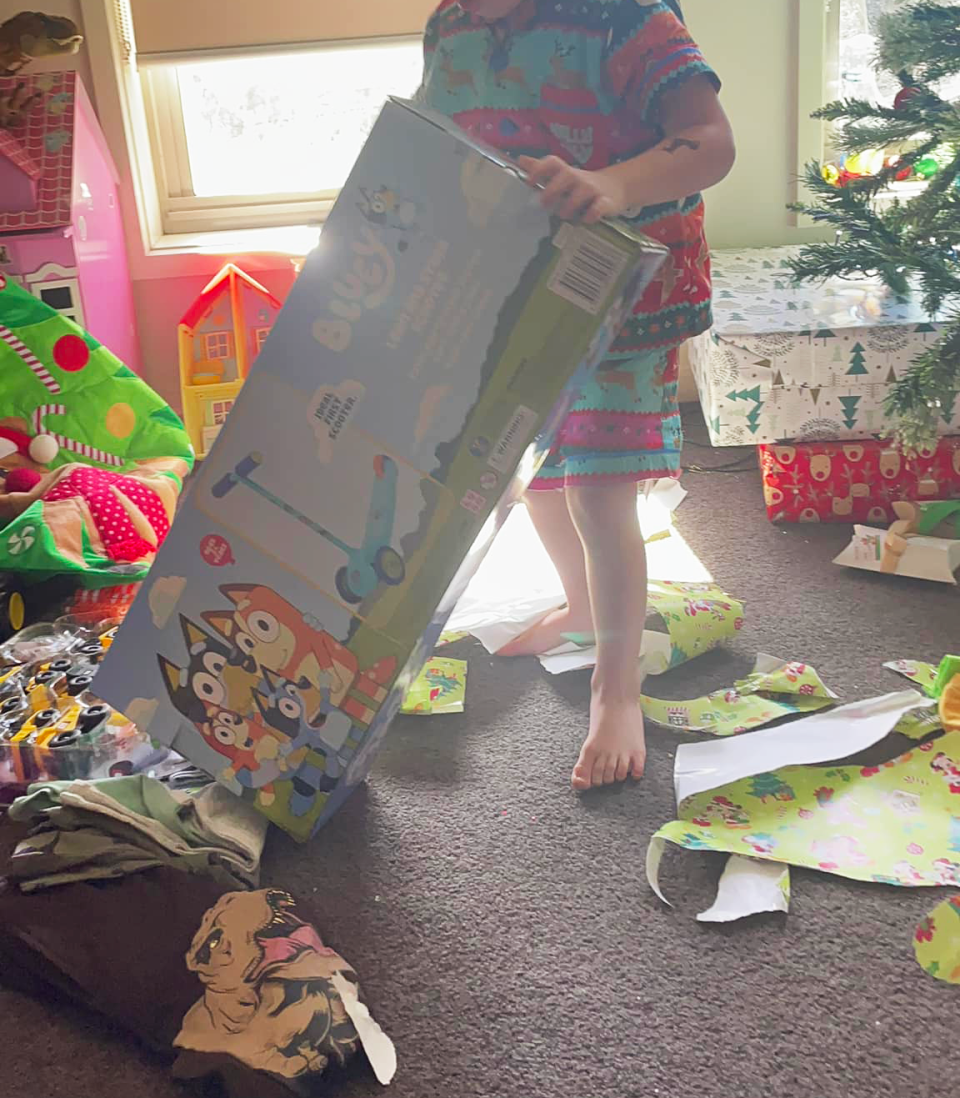 A boy unwrapping a Bluey scooter on Christmas Day.