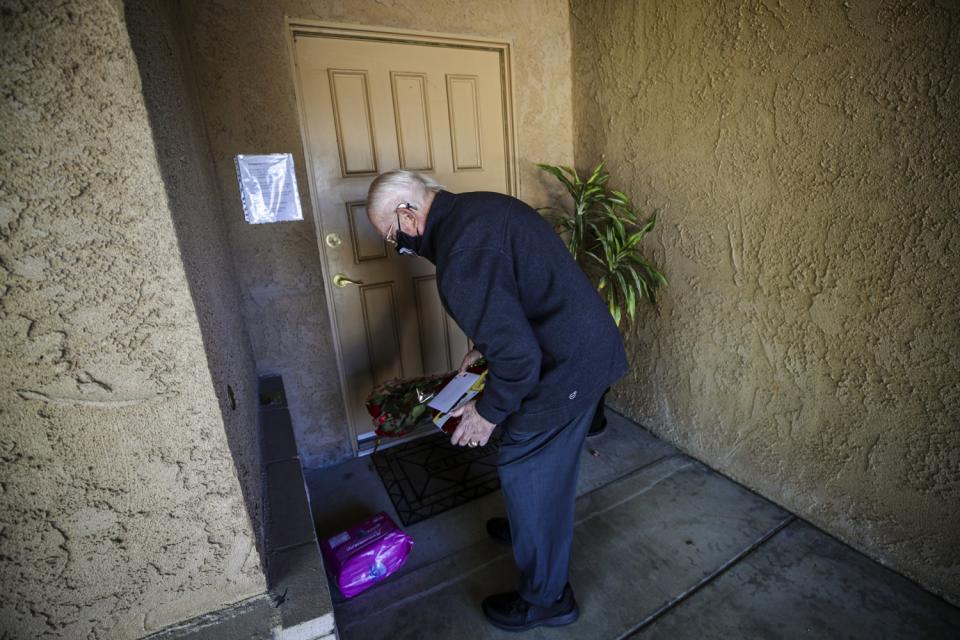 A man bends over to leave a card, flowers and other items on a doorstep