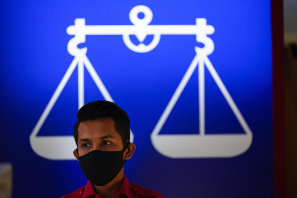 A man wearing a face mask to help curb the spread of the coronavirus stands in front of National Front coalition poster at UMNO headquarter in Kuala Lumpur, Malaysia, Monday, Oct. 26, 2020. A key ally has reaffirmed support for Malaysian Prime Minister Muhyiddin Yassin's government, offering him a respite after his failed bid to declare a coronavirus emergency, but his political survival still hangs in the balance. The UMNO, the biggest party in the unelected governing coalition was angry at being sidelined amid rivalry with Muhyiddin's own Malay party. (AP Photo/Vincent Thian)