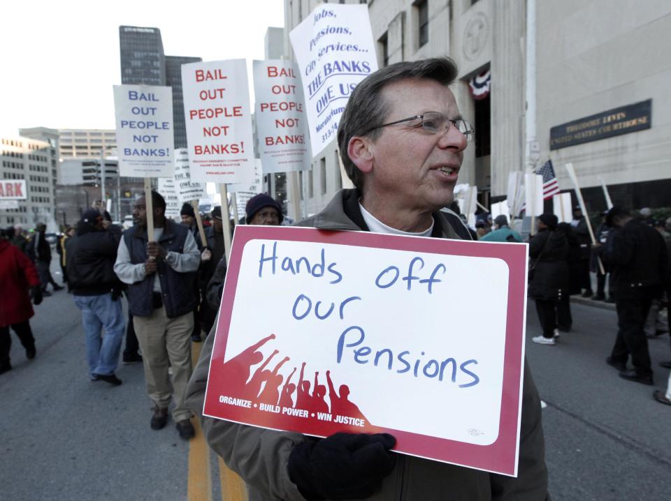 FILE- In this Oct. 23, 2013 file photo, Dennis Marton walks with protesters at a rally outside The Theodore Levin United States Courthouse in Detroit. The city of Detroit reached tentative agreements to preserve pensions for retired police office and firefighters but cut monthly payments for other former employees, officials said Tuesday, April 15, 2014. (AP Photo/Paul Sancya, File)