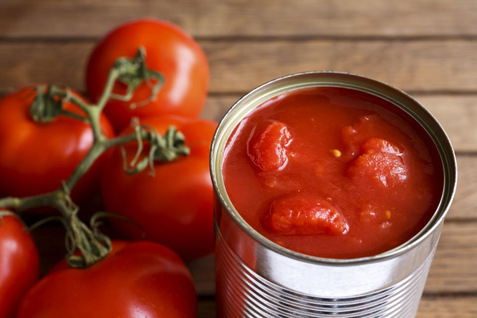 Open tin of chopped tomatoes with whole fresh unfocused tomatoes behind