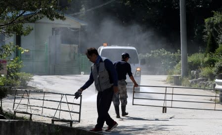 Workers set up a barricade as a vehicle disinfects a pig farm in Yanggu