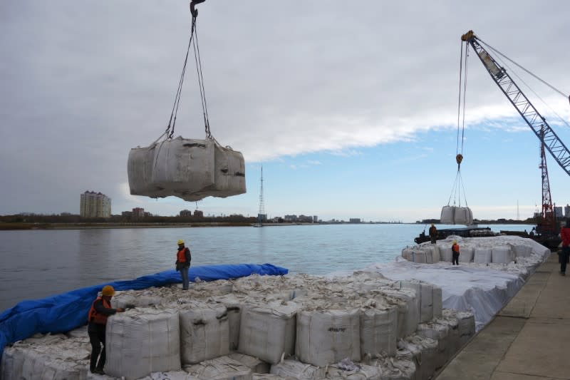 Workers stand near a crane unloading sacks of imported soybeans from Russia at Heihe port in Heilongjiang