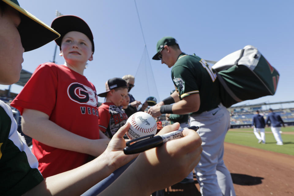 A fan waits with a ball and pen for an autograph as Oakland Athletics' Sean Murphy signs behind before a spring training baseball game against the Seattle Mariners Saturday, March 7, 2020, in Peoria, Ariz. (AP Photo/Elaine Thompson)