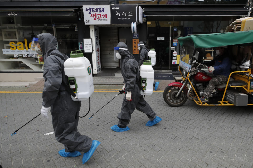 Health officials from the district office wearing protective gears disinfect as a precaution against the coronavirus as a man wearing a face mask rides a motorcycle in Incheon, South Korea, Thursday, Sept. 17, 2020. (AP Photo/Lee Jin-man)