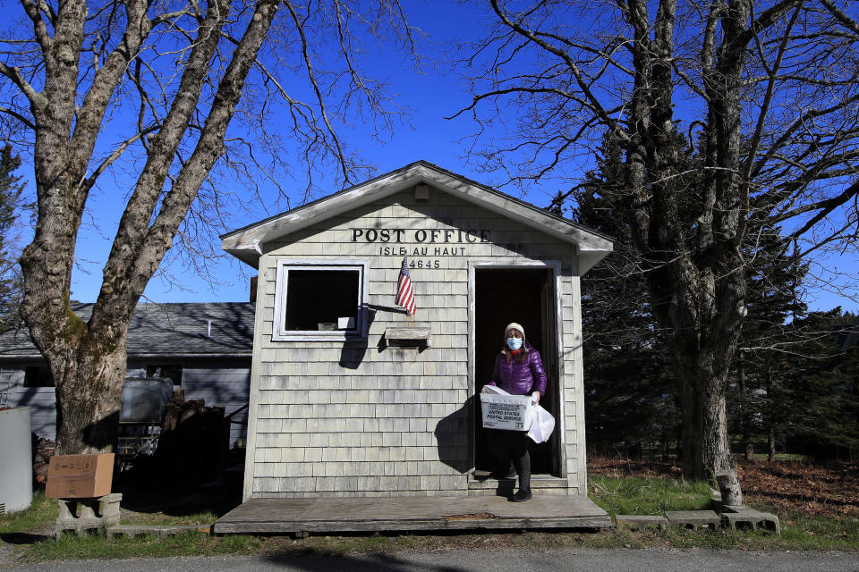 In this Wednesday, May 6, 2020, photo, Postmistress Donna DeWitt carries mail at the tiny post office on Isle Au Haut, Maine. The post office serves the 70 or so year-round island residents. (AP Photo/Robert F. Bukaty)