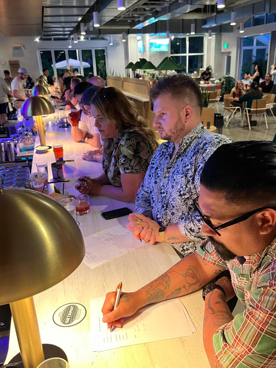 A panel of three judges, Rebecca Monday, background; Nick Ansara, center; and Bert Chavez, foreground, take notes while sampling the original cocktails of six bartenders and contestants June 13 in the Dublin Cocktail Classic at The Getaway Brewing Co.