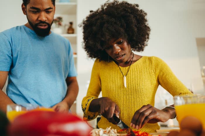 A woman is chopping vegetables in the kitchen at home while a man is standing next to her