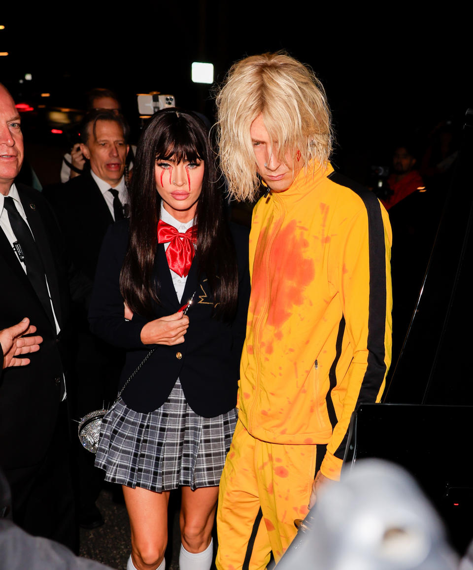 Megan Fox and Machine Gun Kelly arriving at an event, Fox in a plaid skirt and black top, Kelly in a yellow and orange outfit