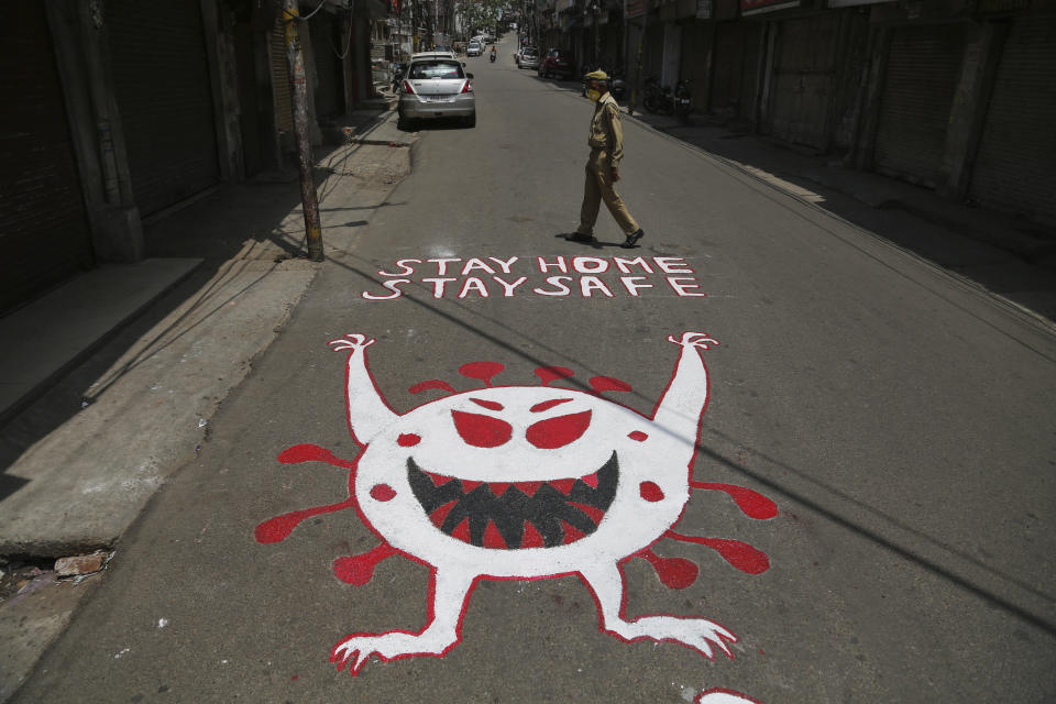 An Indian police man walks past an awareness message painted on a road during a curfew to curb the spread of coronavirus in Jammu, India, Wednesday, May 19, 2021. India has the second-highest coronavirus caseload after the U.S. with more than 25 million confirmed infections.(AP Photo/Channi Anand)