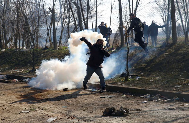 A migrant throws a tear gas canister back during clashes with Greek police, at the Turkey's Pazarkule border crossing with Greece's Kastanies, in Edirne