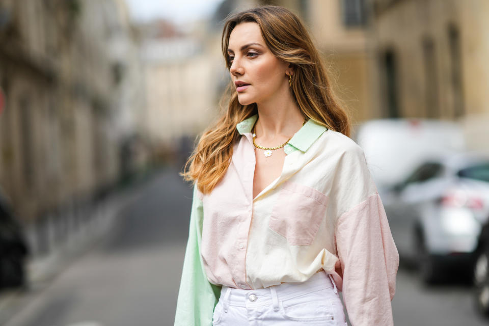 La modelo Olesya Senchenko lleva pendientes grandes de oro, una cadena de oro con un collar de colgantes de flores de margarita, una camisa de yugo de color verde pálido / amarillo / rosa, pantalones vaqueros grandes acampanados de mezclilla blanca, el 4 de agosto de 2021 en París, Francia. (Foto de Edward Berthelot / Getty Images)