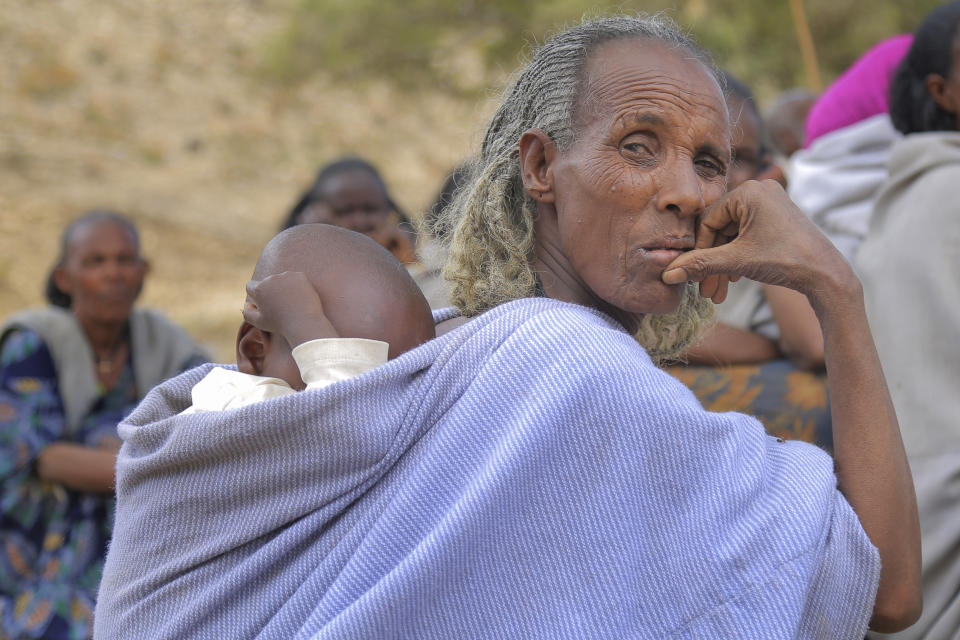 An elderly woman carries a baby on her back as she attends a community meeting in Mai Mekden, in the Tigray region of northern Ethiopia, on Tuesday, Feb. 27, 2024. Once-lush fields lie barren. Mothers, faces etched with worry, watch helplessly as their children weaken from malnutrition. The Ethiopian region of Tigray is peaceful but war’s effects linger, compounded by drought and a level of aid mismanagement that caused the U.N. and the U.S. to temporarily suspend deliveries last year. (AP Photo/Tesfalem Girmay Assefa)