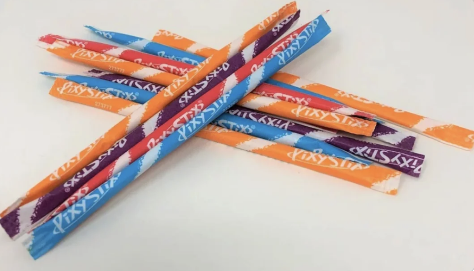 Assorted Pixy Stix candy straws scattered on a white surface
