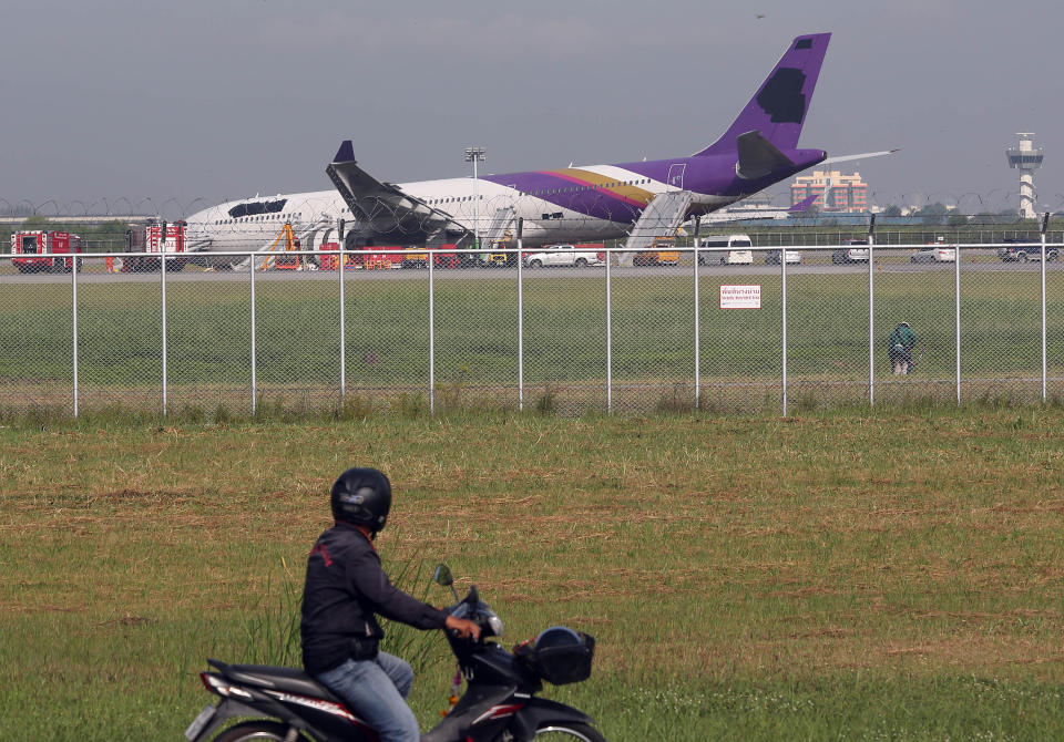 A motorcyclist looks at a damaged Thai Airways Airbus A330-300 at Sunvarnabhumi International Airport in Bangkok, Thailand Monday, Sept. 9, 2013. The plane carrying more than 280 people skidded off the runway while landing Sunday, injuring 14 passengers. After the accident, workers on a crane blacked out the Thai Airways logo on the tail and body of the aircraft. (AP Photo/Apichart Weerawong)