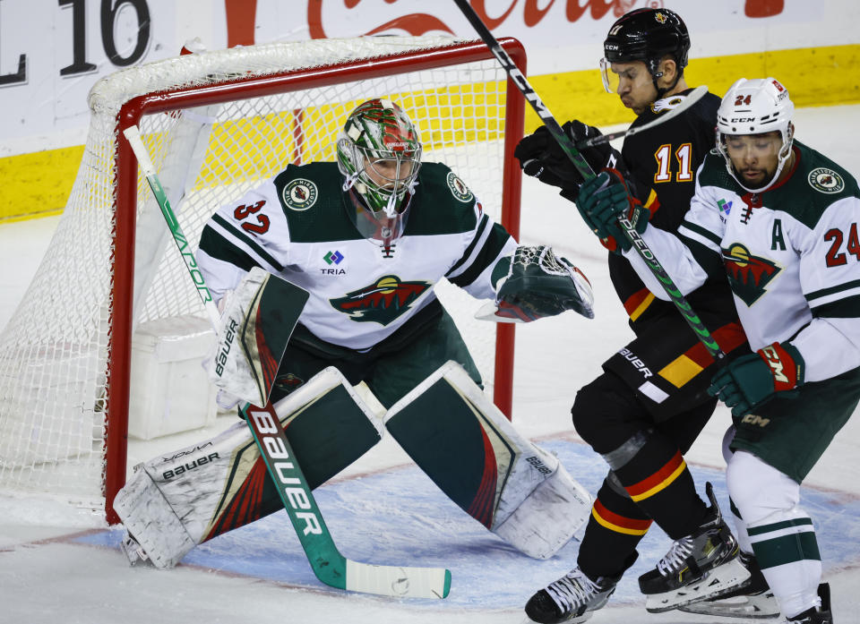 Minnesota Wild defenseman Matt Dumba, right, checks Calgary Flames forward Mikael Backlund, centrer, in front of goalie Filip Gustavsson during the first period of an NHL hockey game Saturday, March 4, 2023, in Calgary, Alberta. (Jeff McIntosh/The Canadian Press via AP)