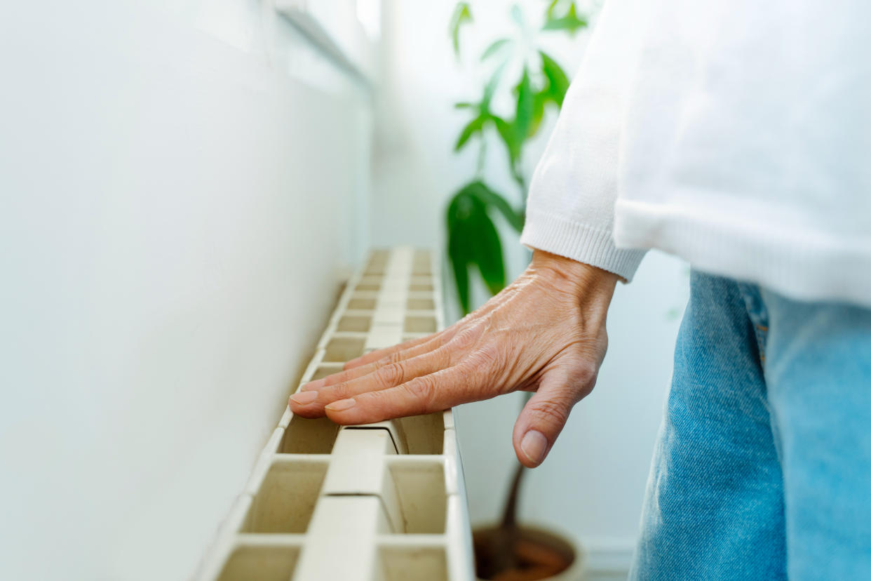 Horizontal close-up view of woman hand touching heat radiator temperature at home with white background