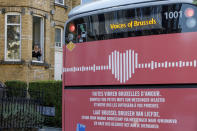 A woman takes a mobile phone photo of a bus delivering a loudspeaker message from family and friends in Brussels, Wednesday, April 22, 2020. With streets in the Brussels capital mostly devoid of loud traffic and honking horns, a simple piece of emotional poetry can split the air. The public bus company, STIB-MIVB, has been calling on people to send in voice messages, which are now delivered by a special bus driving in a loop to connect all the messages and leave a trail of happiness. (AP Photo/Olivier Matthys)