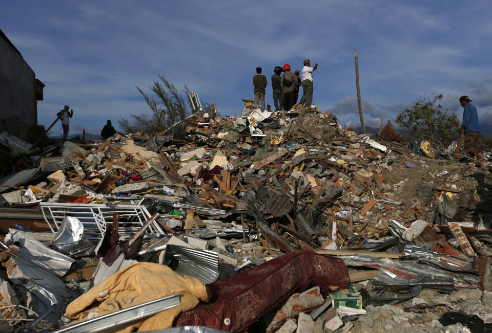 In this Sunday, Oct. 7, 2018, photo, people stand on top of rubble and dried mud as they survey the damage of the Petobo neighborhood which was wiped out by earthquake-triggered liquefaction in Palu, Central Sulawesi, Indonesia. Many in the decimated village had no idea they were in an area already identified as a high-risk zone for this apocalyptic phenomenon that causes soft ground to liquefy during temblors. The area around Sulawesi island's Palu Bay had been slammed before and was due for another potential perfect storm, capable of unleashing earthquakes, landslides, tsunami waves, and soil liquefaction. (AP Photo/Dita Alangkara)