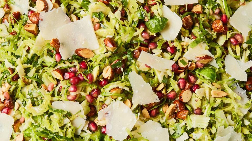 shaved brussels sprouts with pomegranates, shaved parmesan, and chopped toasted almonds in a white bowl