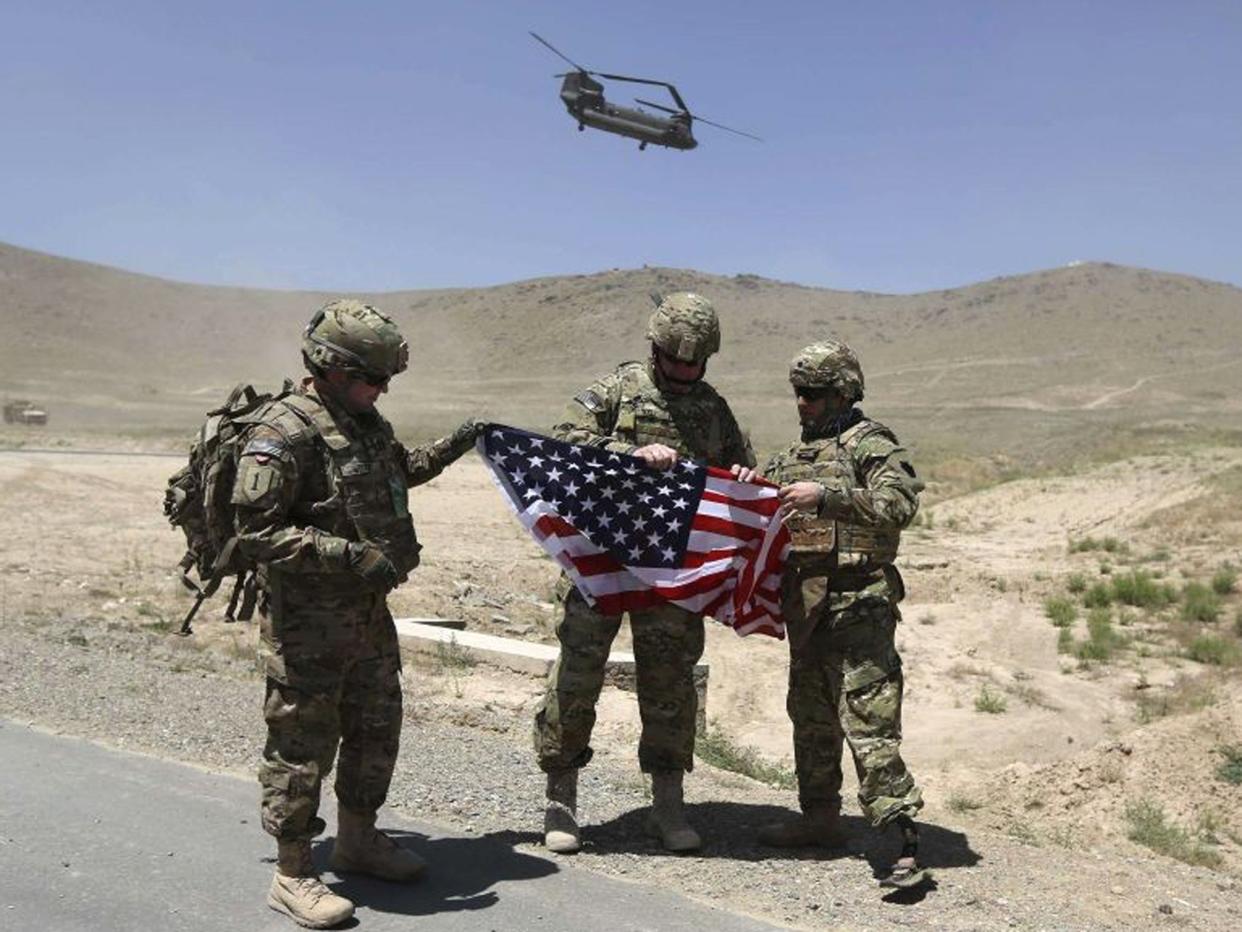 Nato soldiers stand with US flag as a Chinook helicopter takes off after a security handover ceremony at a military academy outside Kabul (Reuters)