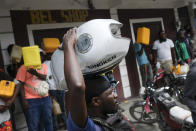 A man balances his motorbike tank on his head as he waits outside a gas station in hopes of filling his tank, in Port-au-Prince, Haiti, Saturday, Oct. 23, 2021. The ongoing fuel shortage has worsened, with demonstrators blocking roads and burning tires in Haiti's capital to decry the severe shortage and a spike in insecurity. (AP Photo/Matias Delacroix)