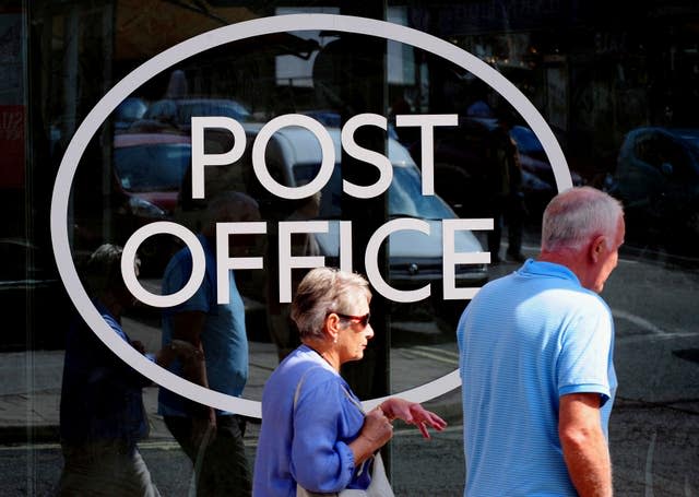 People walk past a Post Office sign