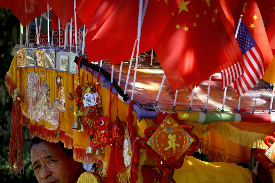 FILE - In this Sept. 16, 2018, file photo, a driver looks out from his trishaw decorated with an American flag and Chinese flags in Beijing. China's economy czar and the U.S. Treasury secretary discussed plans for talks on a tariff battle, the government said Tuesday, Dec. 11, 2018, indicating negotiations are going ahead despite tension over the arrest of a Chinese tech executive. (AP Photo/Andy Wong, File)