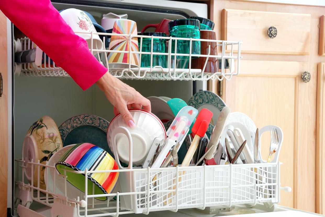 female hand is shown loading dishes into full dishwasher