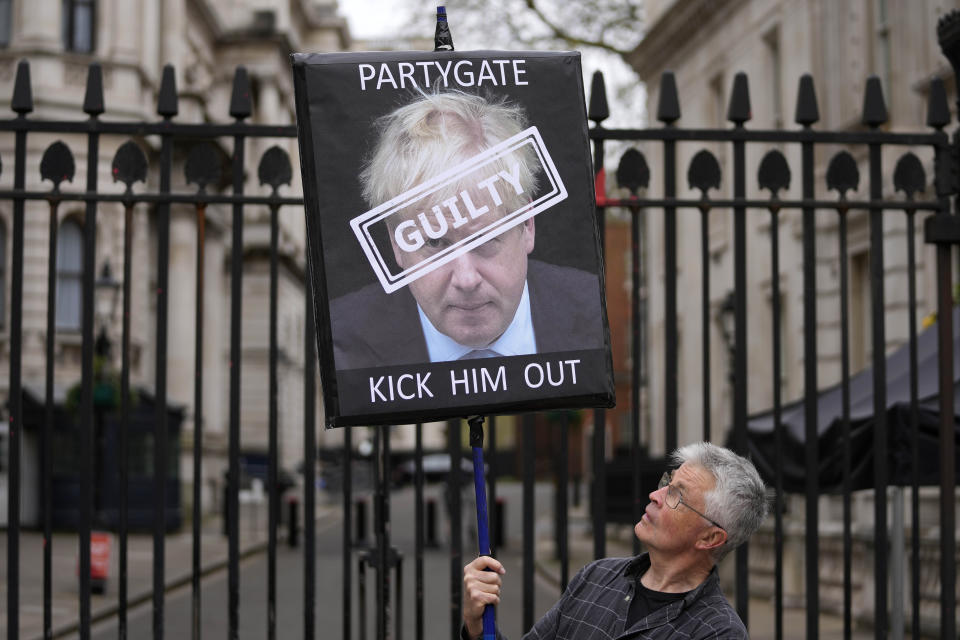 FILE - A protester holds a sign showing British Prime Minister Boris Johnson as he stands in front of the entrance to Downing Street in London, Wednesday, April 13, 2022. Former Prime Minister Boris Johnson deliberately misled Parliament about the lockdown-flouting parties that undermined his credibility and contributed to his downfall, a committee of lawmakers said Thursday, June 15, 2023 after a year-long investigation. (AP Photo/Frank Augstein, File)