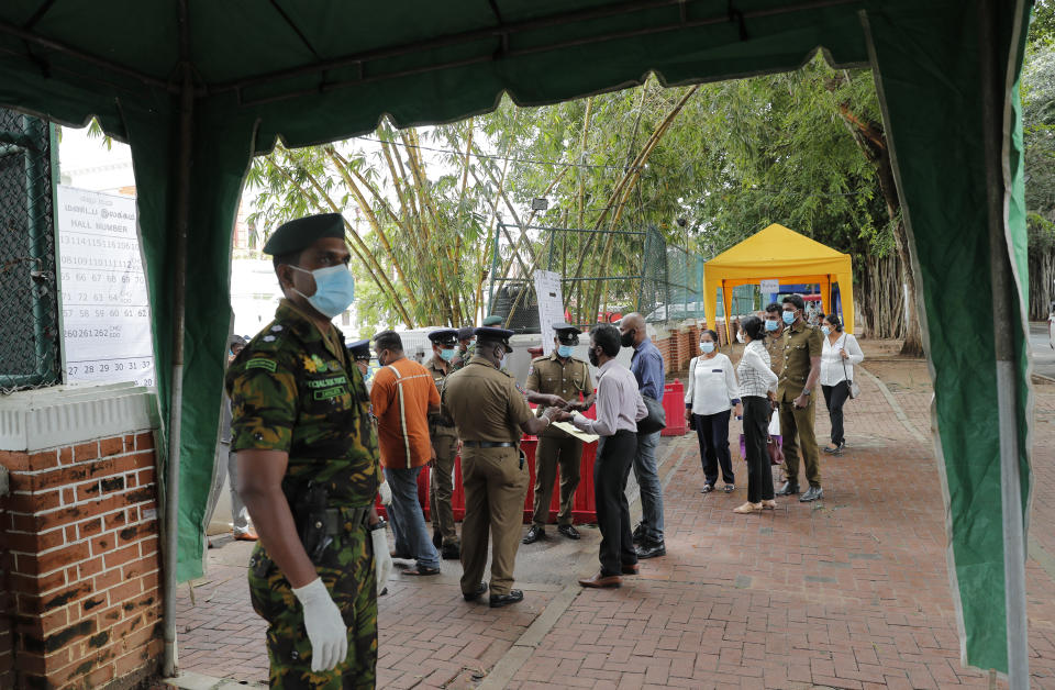 A Sri Lankan government soldier stands guard at the entrance to a ballot counting center as workers show their identity to police officers, a day after voting for general elections in Colombo, Sri Lanka, Thursday, Aug. 6, 2020. (AP Photo/Eranga Jayawardena)