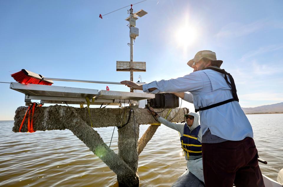 Ryan G. Sinclair, Loma Linda University associate professor of public health and earth and biological sciences, cleans off a solar panel that powers a hydrogen sulfide sensor in the Salton Sea, Calif., on Thursday, Dec. 14, 2023. Quinn Montgomery, Alianza consultant biologist, keeps the boat steady. The sensor also measures nitrogen dioxide and volatile organic compounds. Hydrogen sulfide is a toxic gas that smells of rotten eggs. | Kristin Murphy, Deseret News