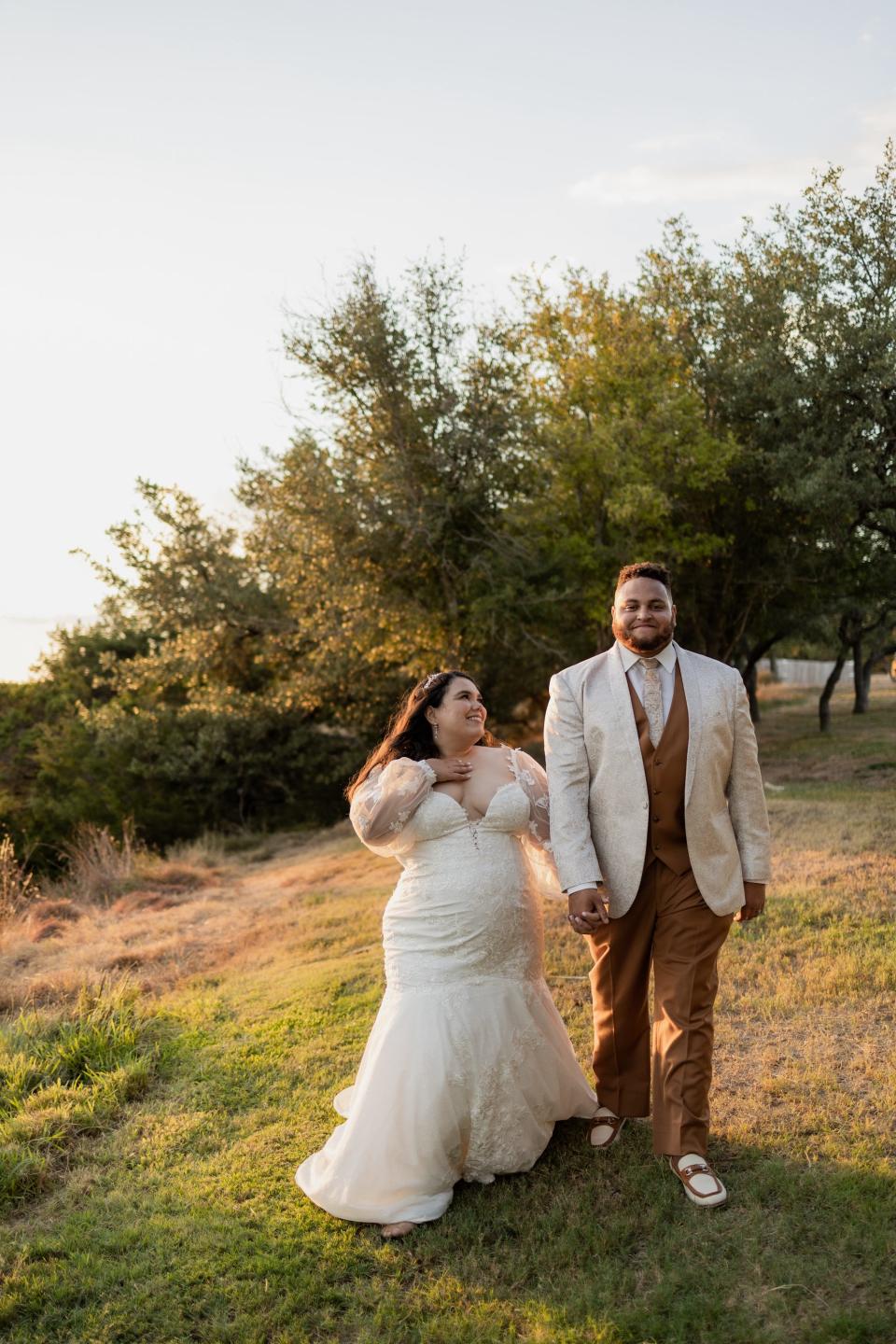 A bride looks at her groom as they walk through a field.