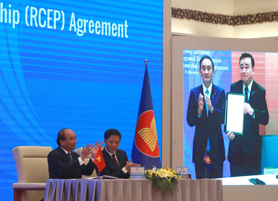 Vietnamese Prime Minister Nguyen Xuan Phuc, left, and Minister of Trade Tran Tuan Anh, right, applaud next to a screen showing Japanese Prime Minister Yoshihide Suga and Minister of Trade Hiroshi Kajiyama holding up signed RCEP agreement, in Haoni, Vietnam. China and 14 other countries have agreed to set up the world's largest trading bloc, encompassing nearly a third of all economic activity, in a deal many in Asia are hoping will help hasten a recovery from the shocks of the pandemic. (AP Photo/Hau Dinh)