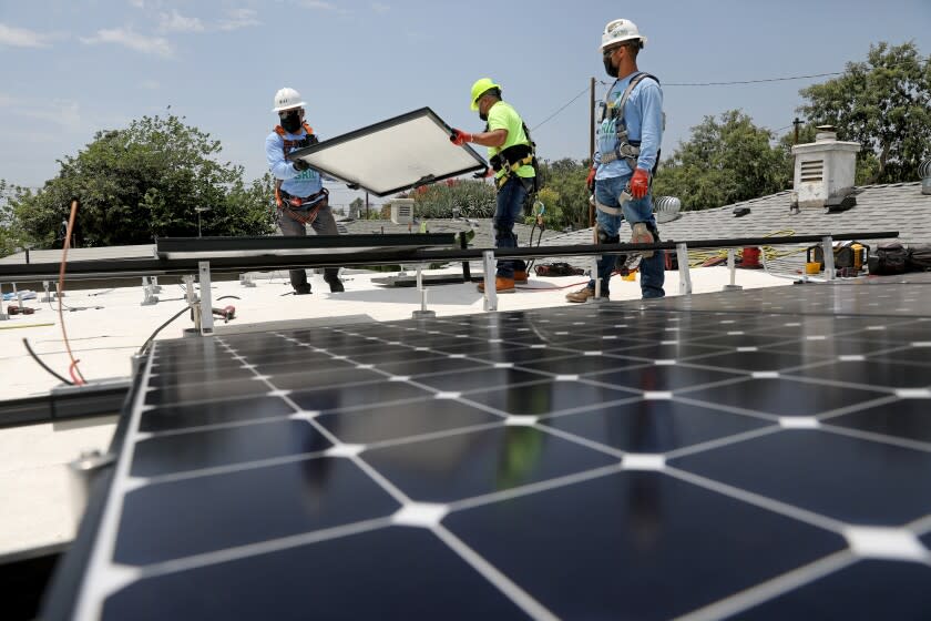 LOS ANGELES, CA - JUNE 18: Lee Kwok, left, solar installer supervisor, Juan Alcantara, intern/trainee, and Sal Miranda, supervisor, of GRID Alternatives, a nonprofit, install solar panels that will generate 5 kilowatts of energy at a low-income home in Watts on Friday, June 18, 2021 in Los Angeles, CA. A total of 15 327 watt panels were placed on the roof. (Gary Coronado / Los Angeles Times)